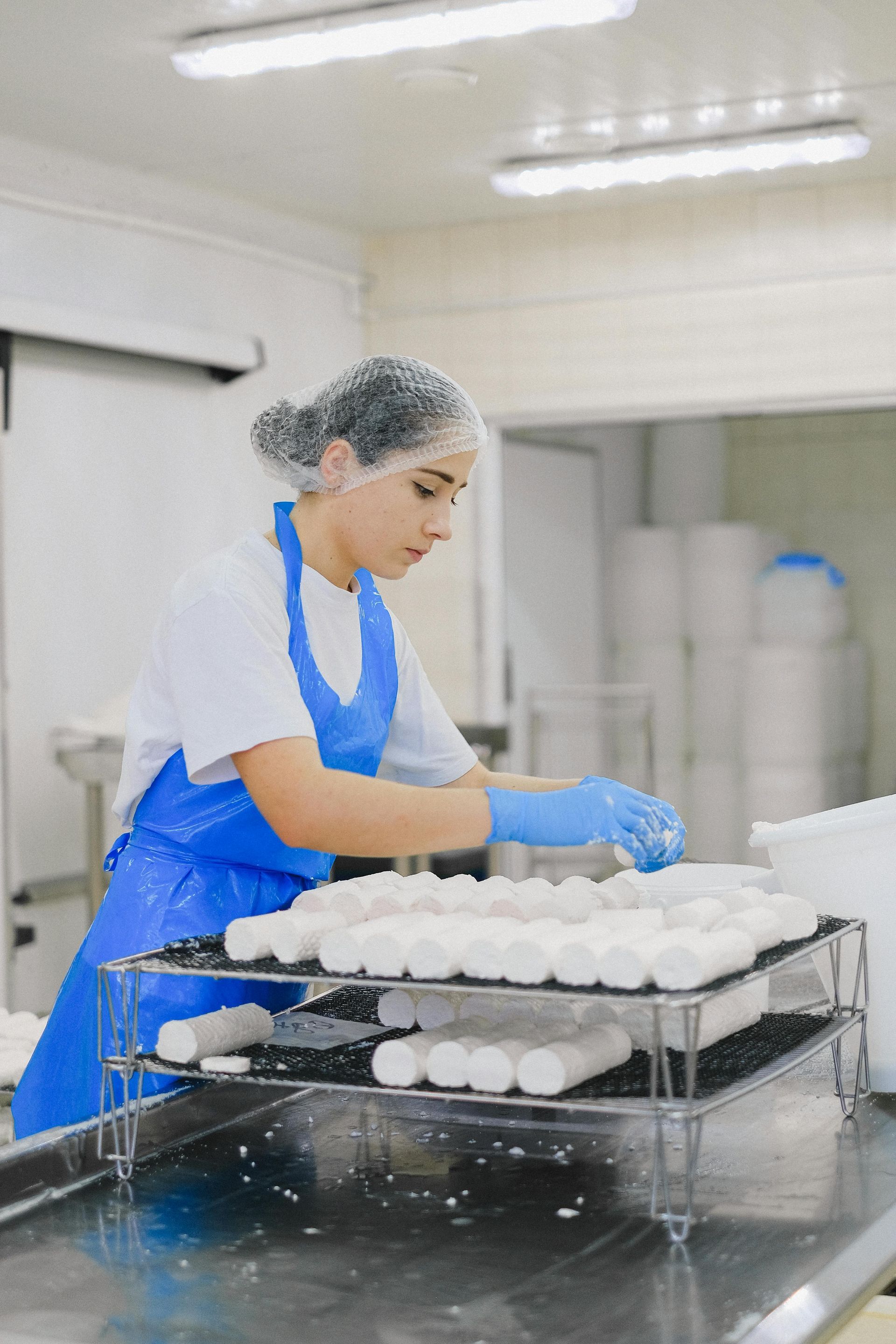 Woman in blue apron and gloves arranging white cheese rolls.