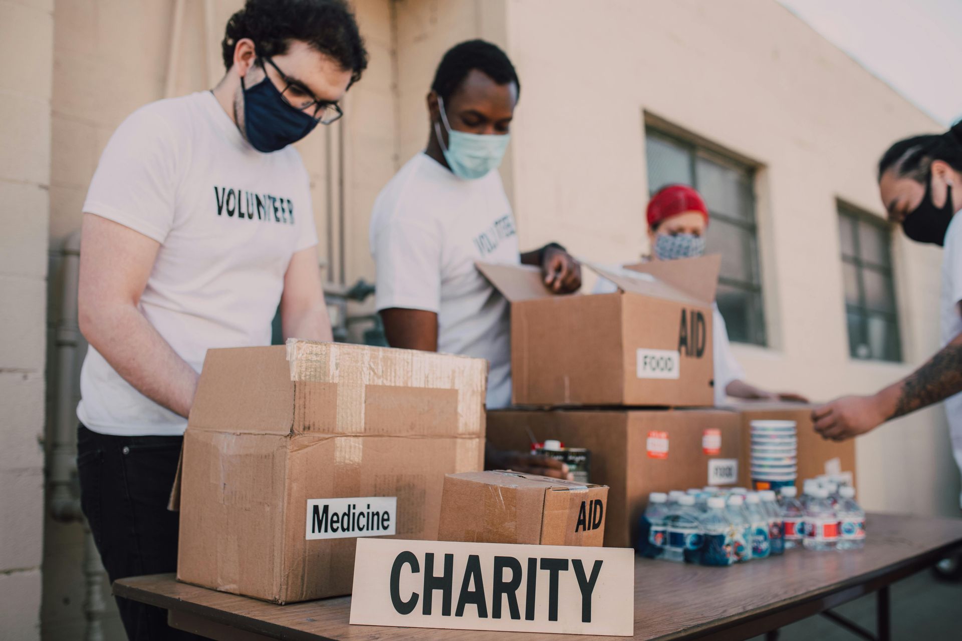 Volunteers pack donation boxes at a charity table with bottled water and supplies