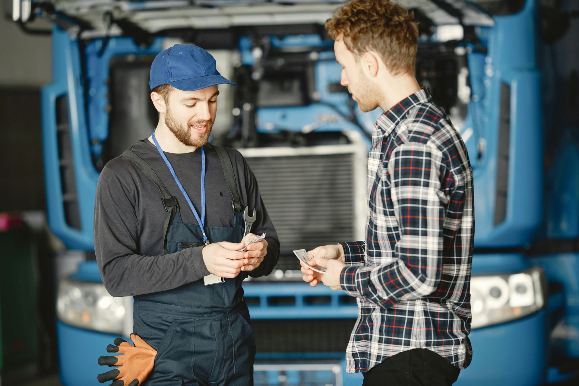 Two mechanics discussing a tool in front of a blue truck garage