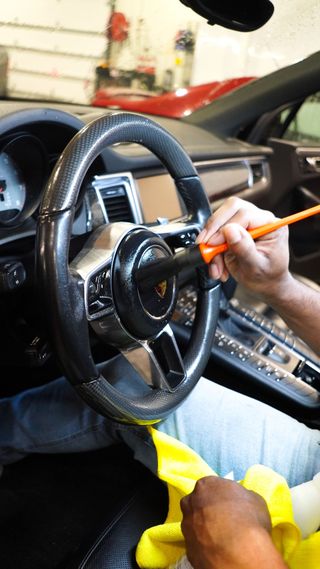 A person is cleaning the steering wheel of a car with a brush.