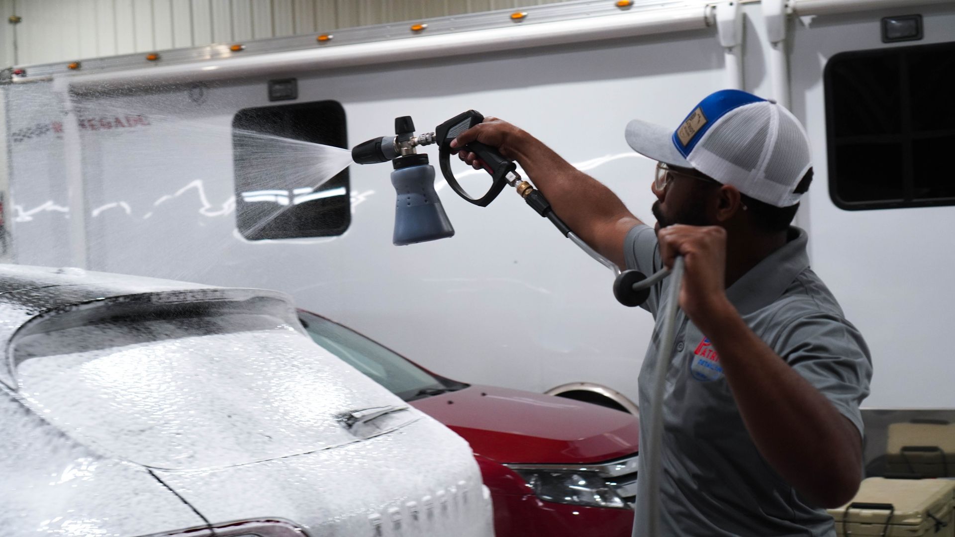 A man is washing a red car with a high pressure washer.