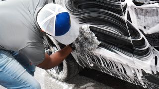 A man wearing a blue hat is washing a car