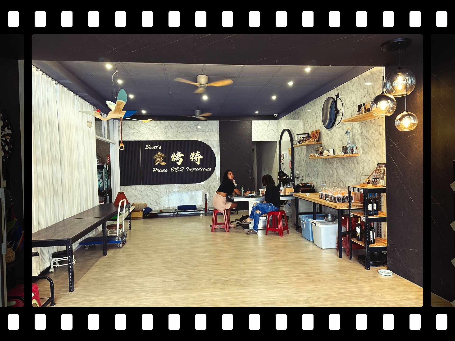 食烤特Scott商店內部。兩個人坐著，其中一個坐在他們前面。商店裡擺放著桌子、燈號和招牌。