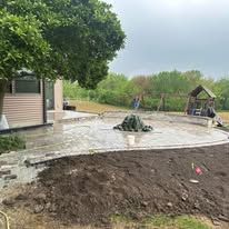 A concrete patio is being built in a backyard with a playground in the background.