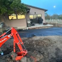 A red excavator is digging a hole in front of a house.