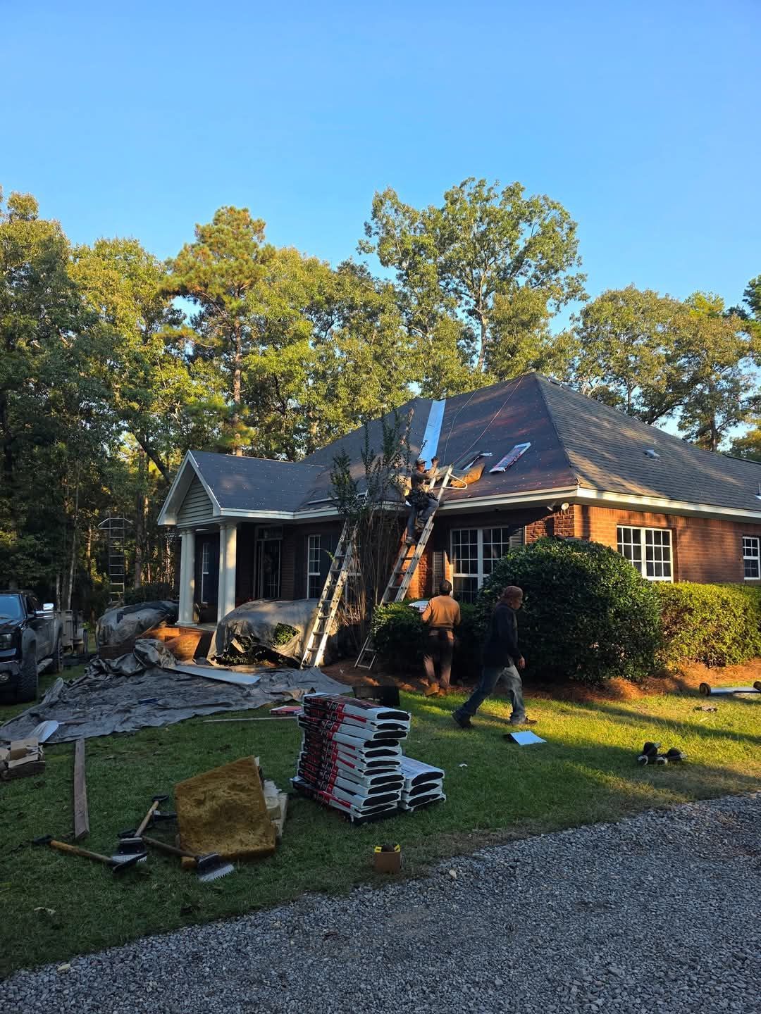 Red brick house with brown shingle roof, tan trim, and blue sky.