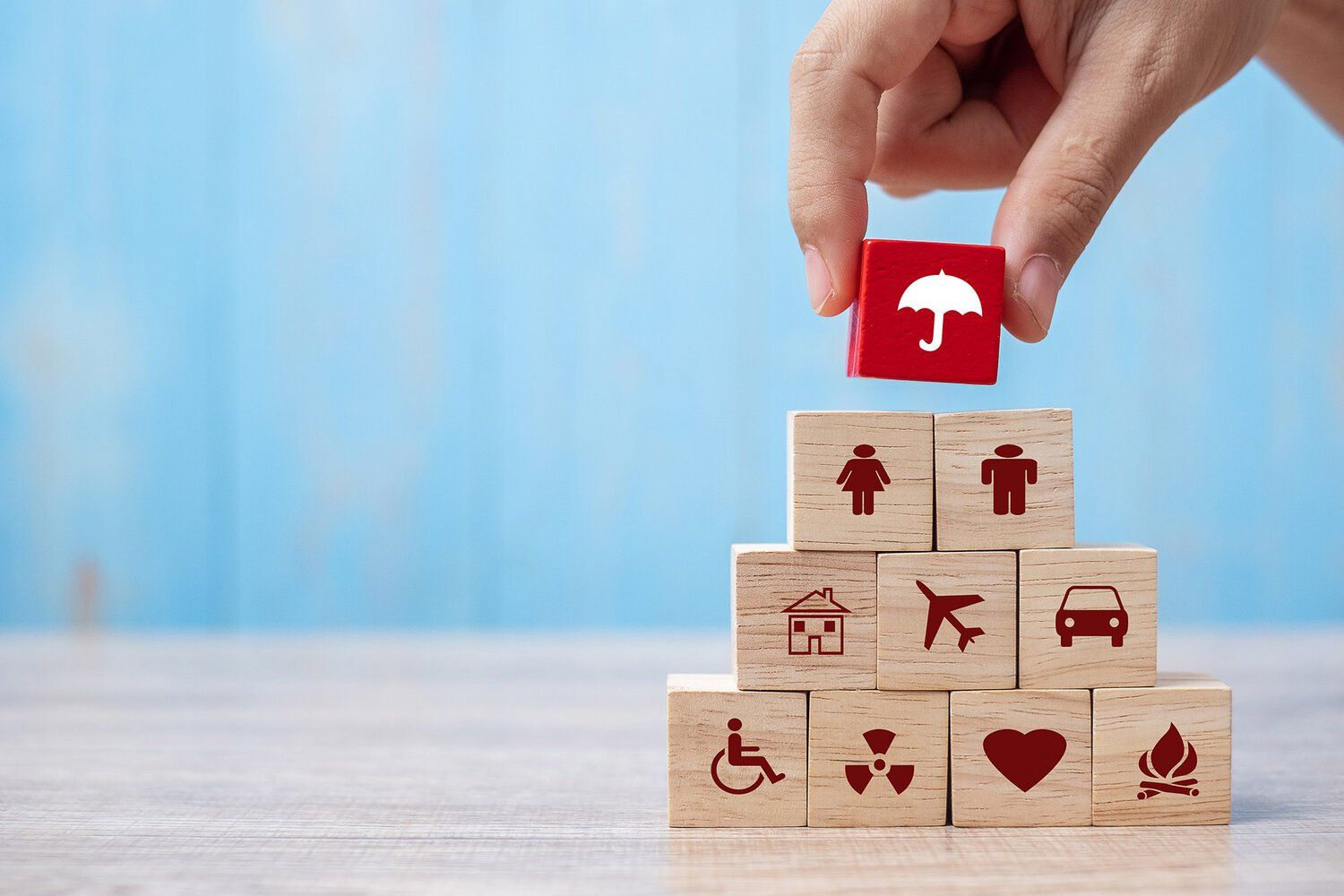 hand stacking blocks with insurance related topics on them, such as home, health, and auto