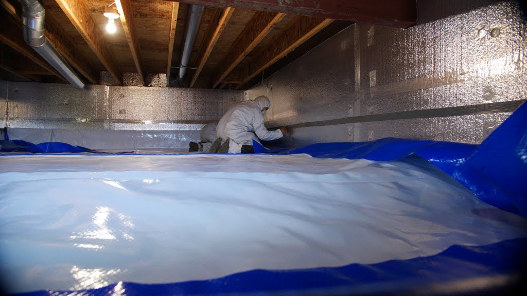 Technician applying crawl space encapsulation with insulation and vapor barrier.
