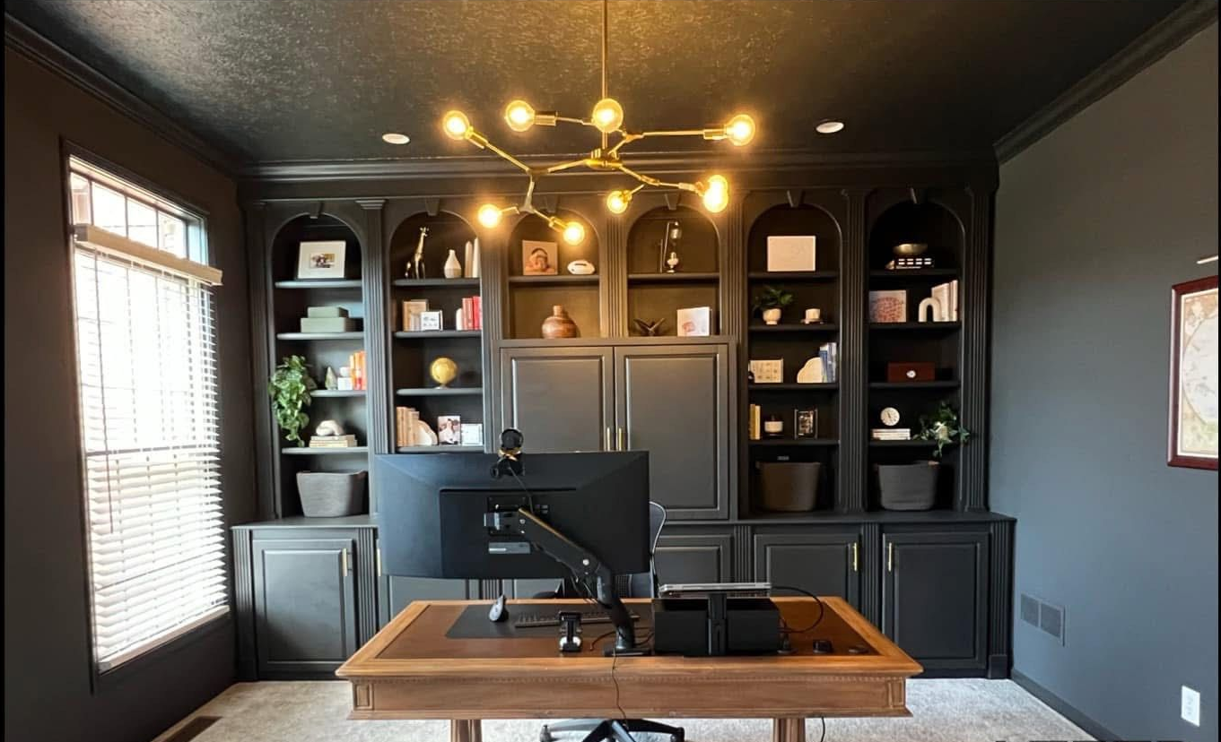 White kitchen cabinets with black hardware, dark wood floor, and arched window with blinds.