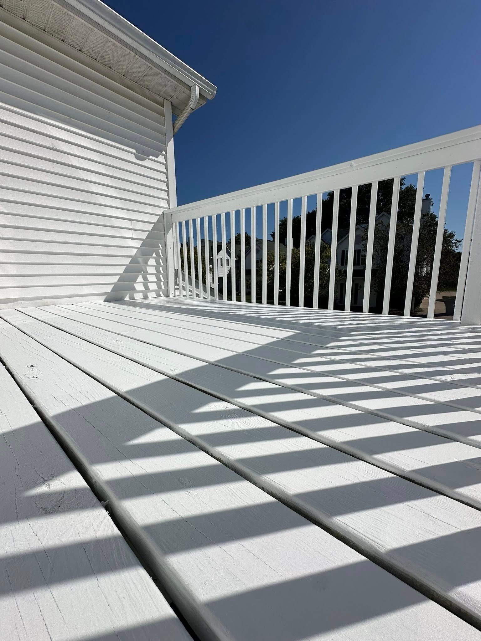 White painted deck with railing against a blue sky. Shadows cast from railing.