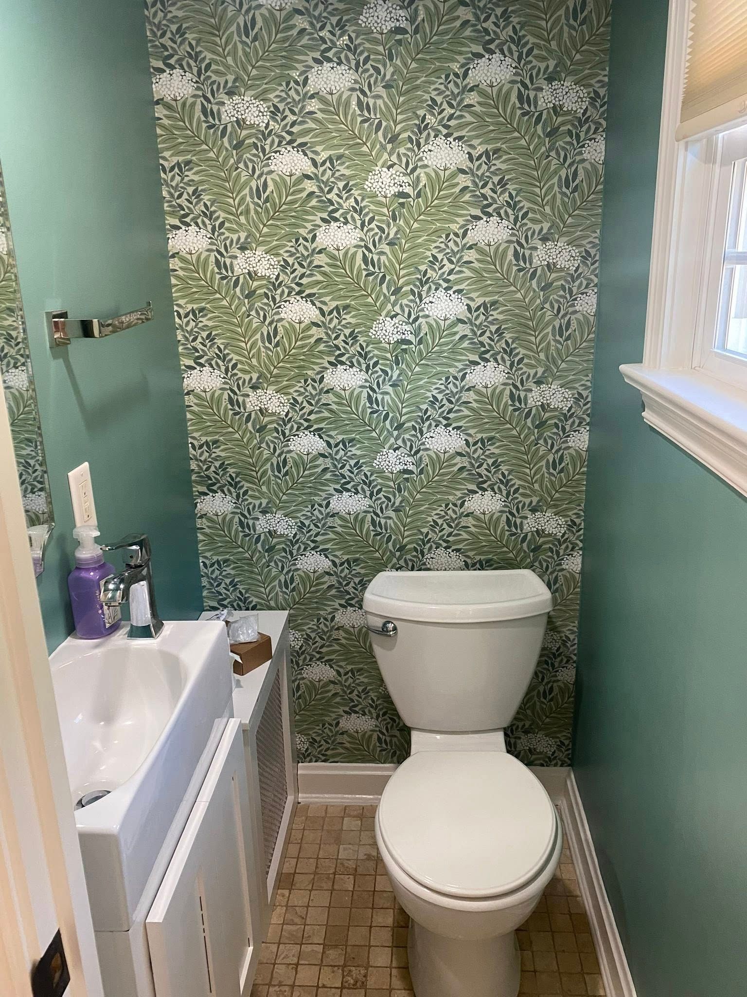 Small bathroom with floral wallpaper, toilet, sink, and turquoise walls.