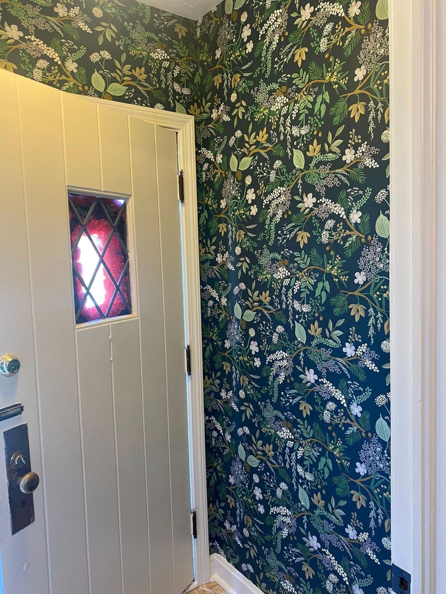A doorway with a cream-colored door and floral wallpaper in a hallway.