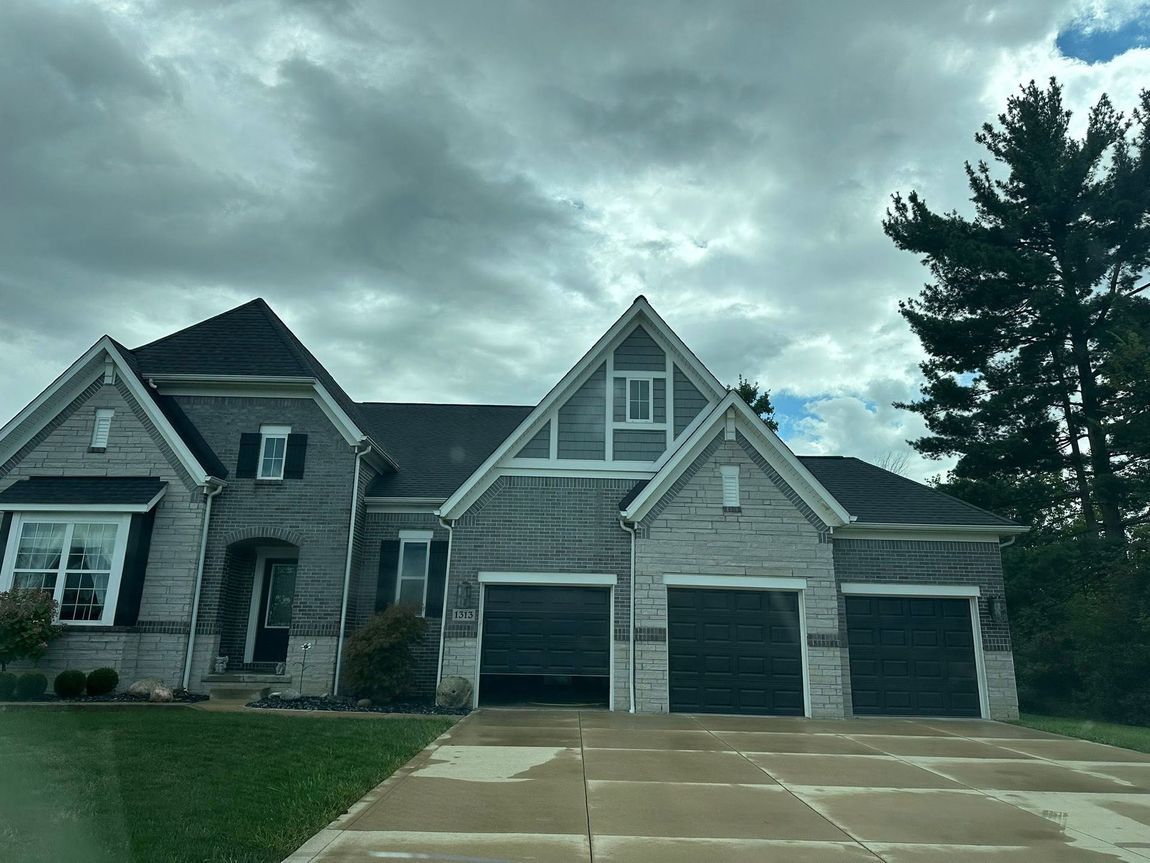 Gray brick house with black garage doors under a cloudy sky.