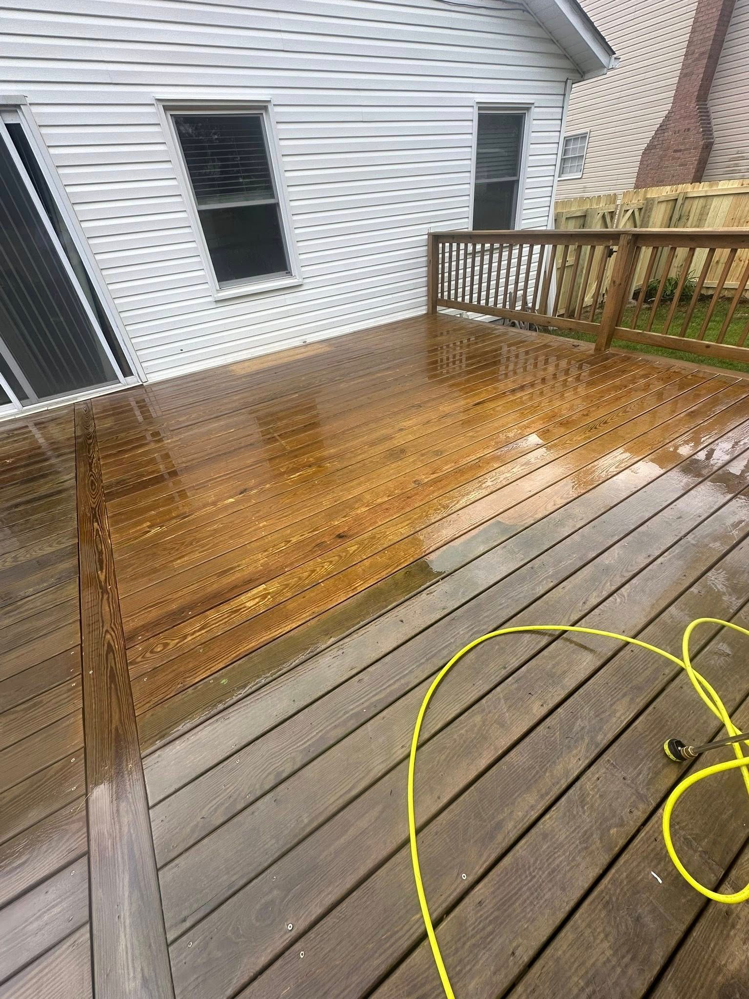 Wet wooden deck with a building in the background. A yellow hose is lying on the deck.