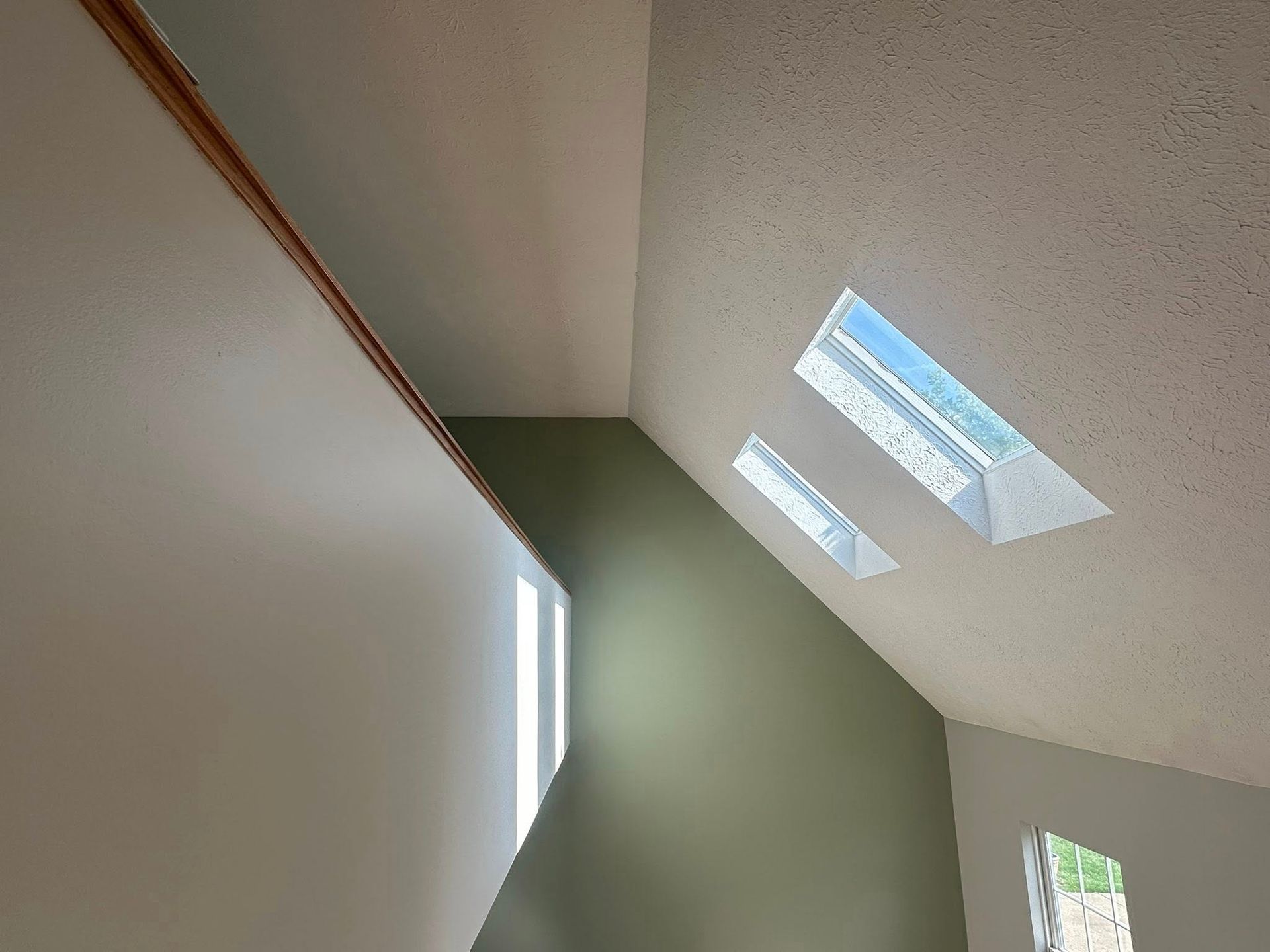 Interior view of a room with angled ceiling, skylights, and a wall painted olive green.