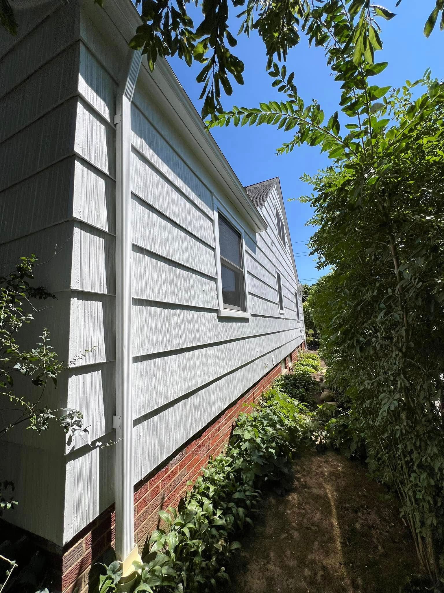 Side of a light blue house with white trim, brick foundation, and a narrow garden path.