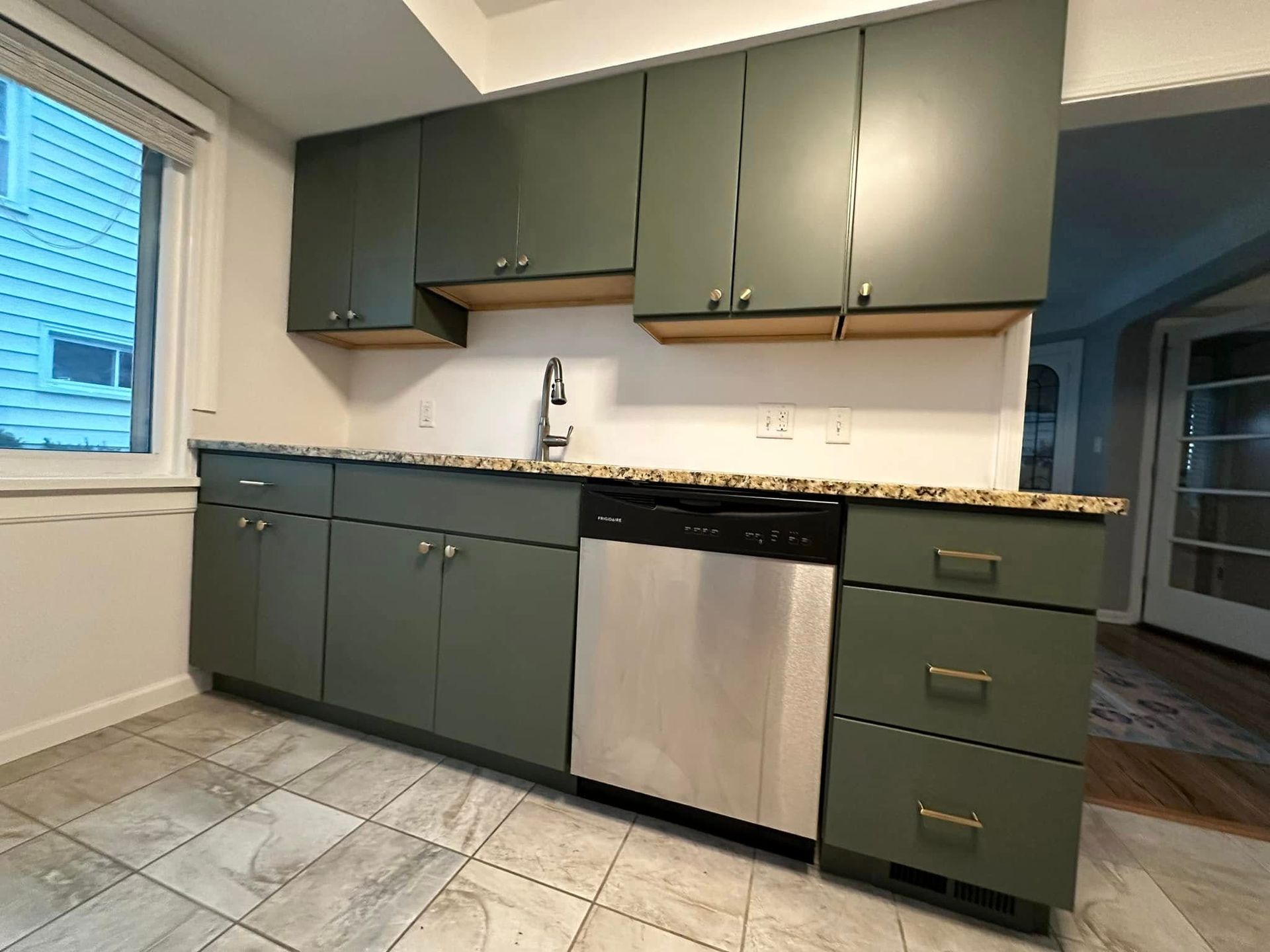 Green kitchen cabinets with granite countertops, stainless steel appliances, and a window.