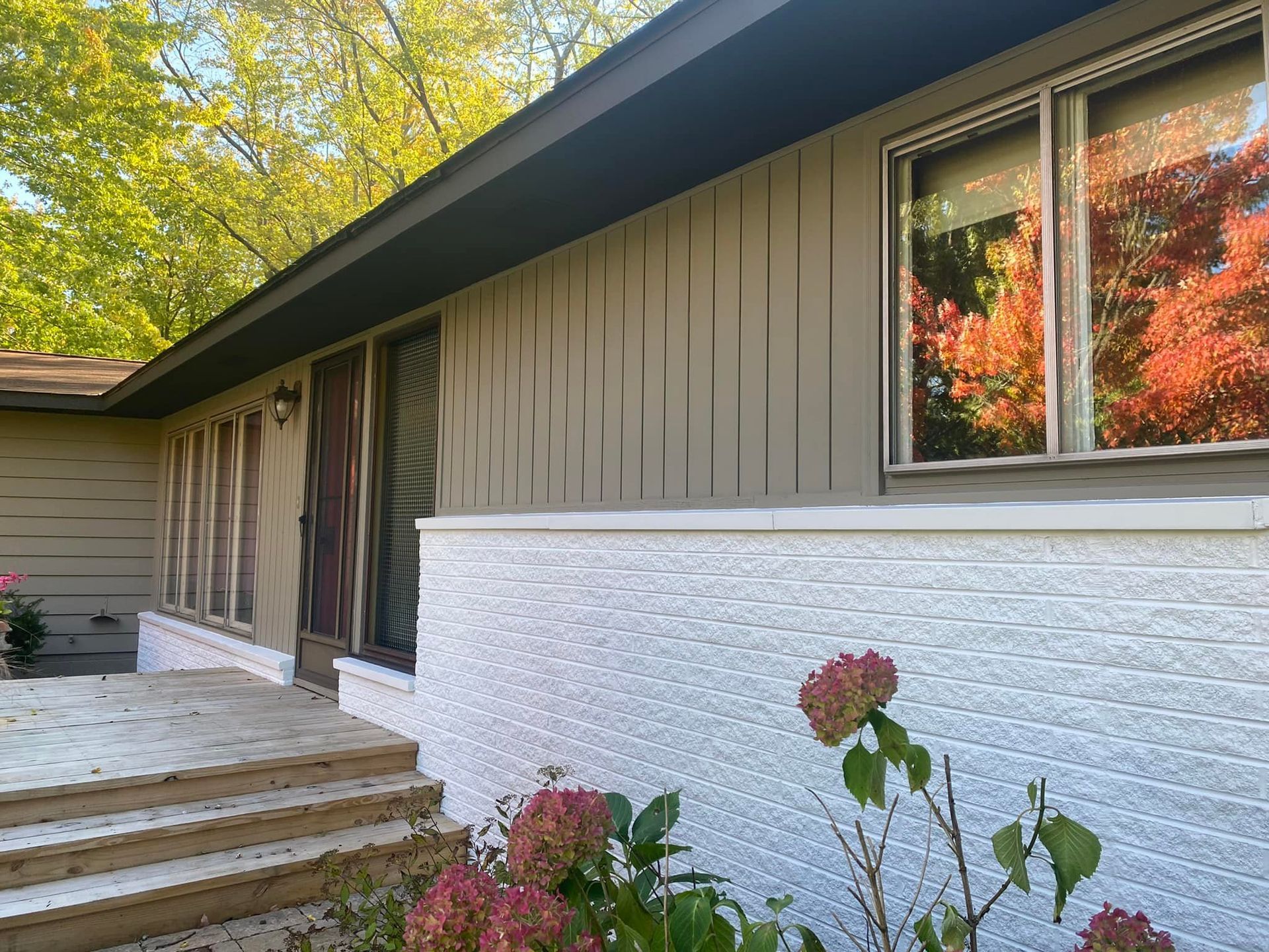 Exterior of a house with white brick, tan siding, and autumn leaves reflected in windows.