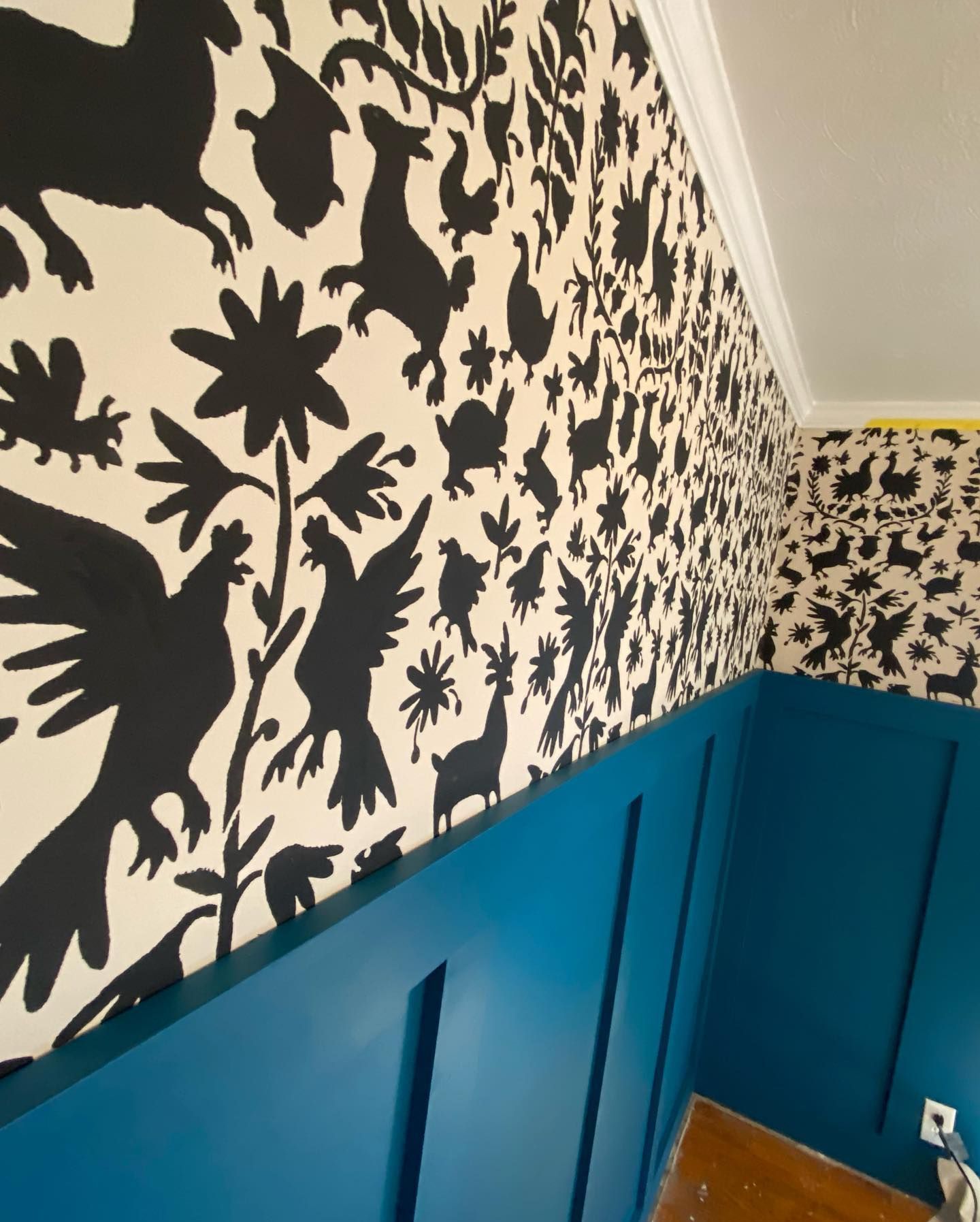 Blue paneled wall with black and white patterned wallpaper.