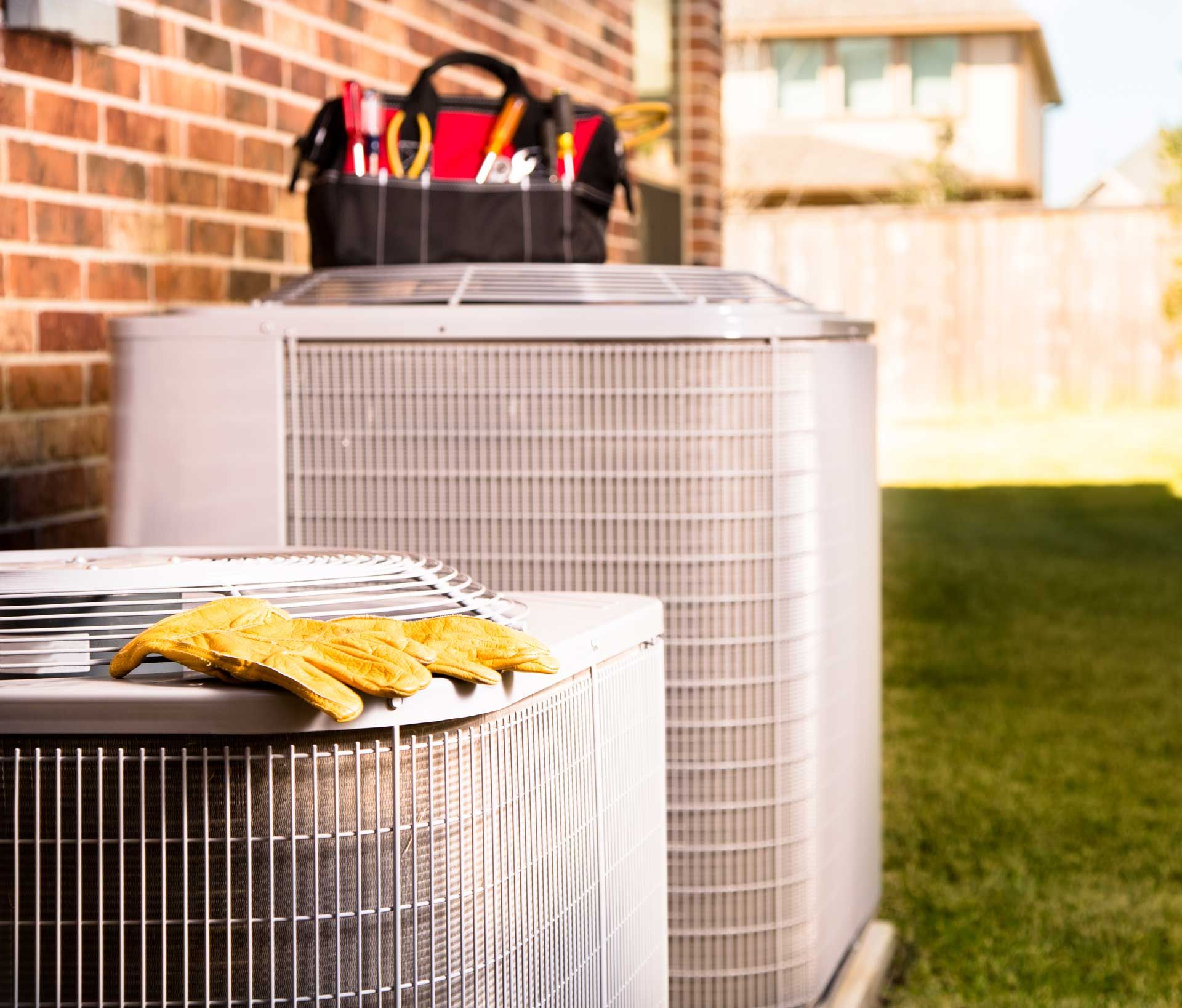 Two air conditioners are sitting next to each other on the side of a brick building.