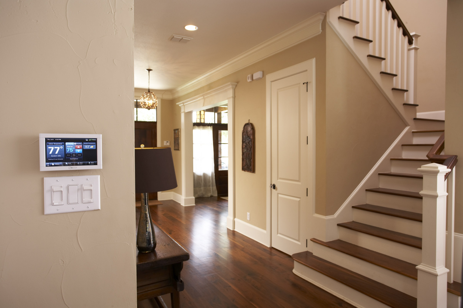 A hallway with stairs and a thermostat on the wall.
