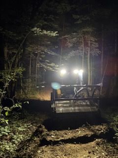 Tractor in dark forest, its lights illuminating a clearing.
