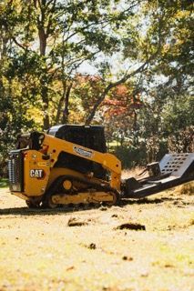Yellow Caterpillar skid steer with attached trailer in a grassy field.