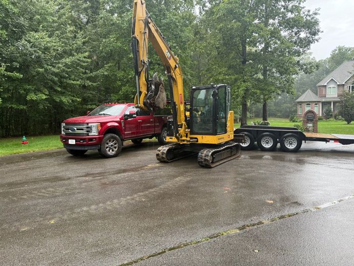 Yellow excavator on gravel pile, digging in a forest setting.