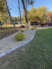 Landscaped garden bed with gray stone and plants, bordered by gray pavers and green grass.