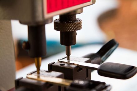 Key-cutting machine in use, duplicating a metal key; close-up shows tools and blades.