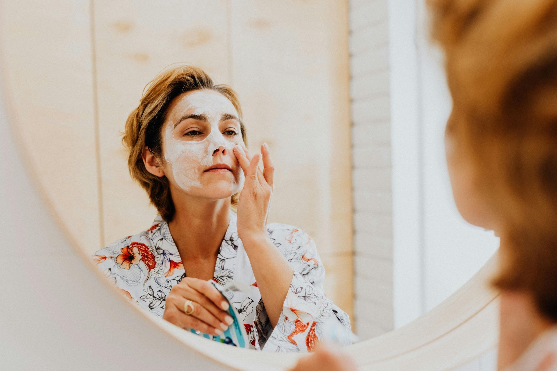 Woman standing in front of mirror, applying cream on her face