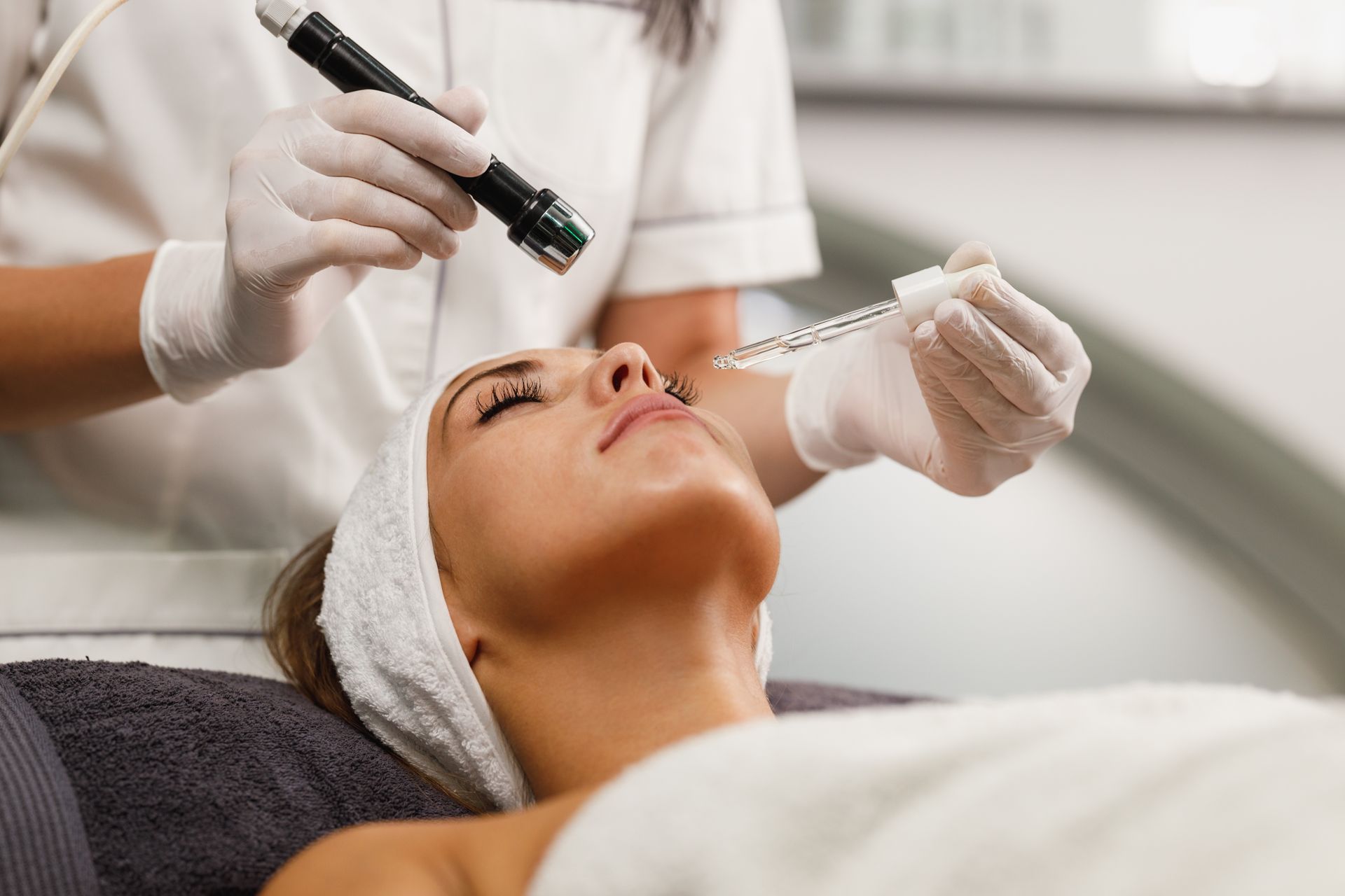Woman receiving facial treatment in spa setting; esthetician applying serum.