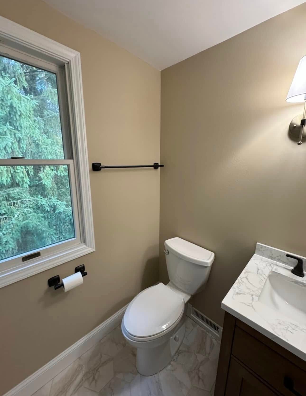 Bathroom with toilet, vanity, window, and towel bar; beige walls, white trim, and natural light.