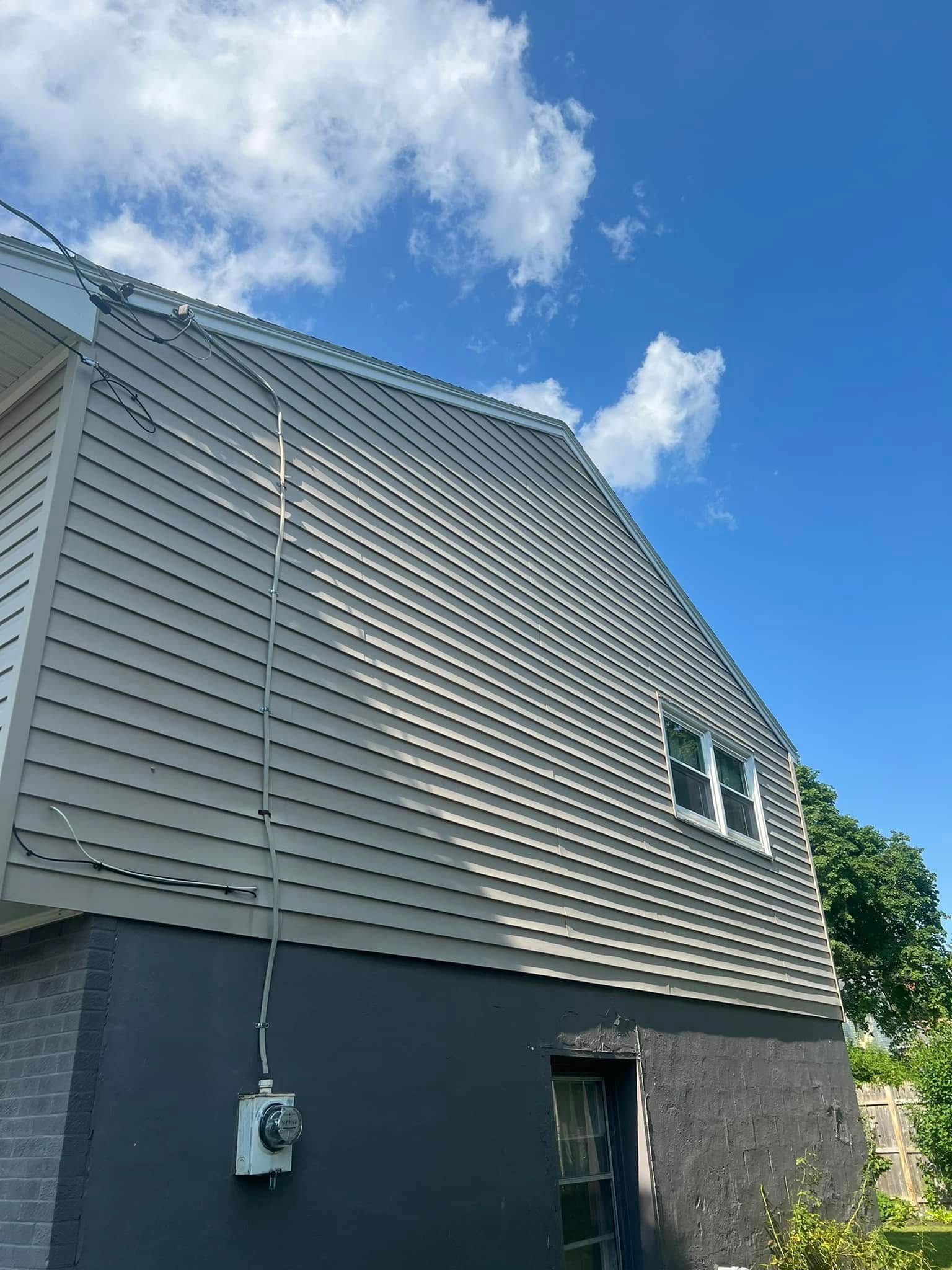 Gray siding on a two-story house with a dark bottom section against a blue sky. Electrical box visible.