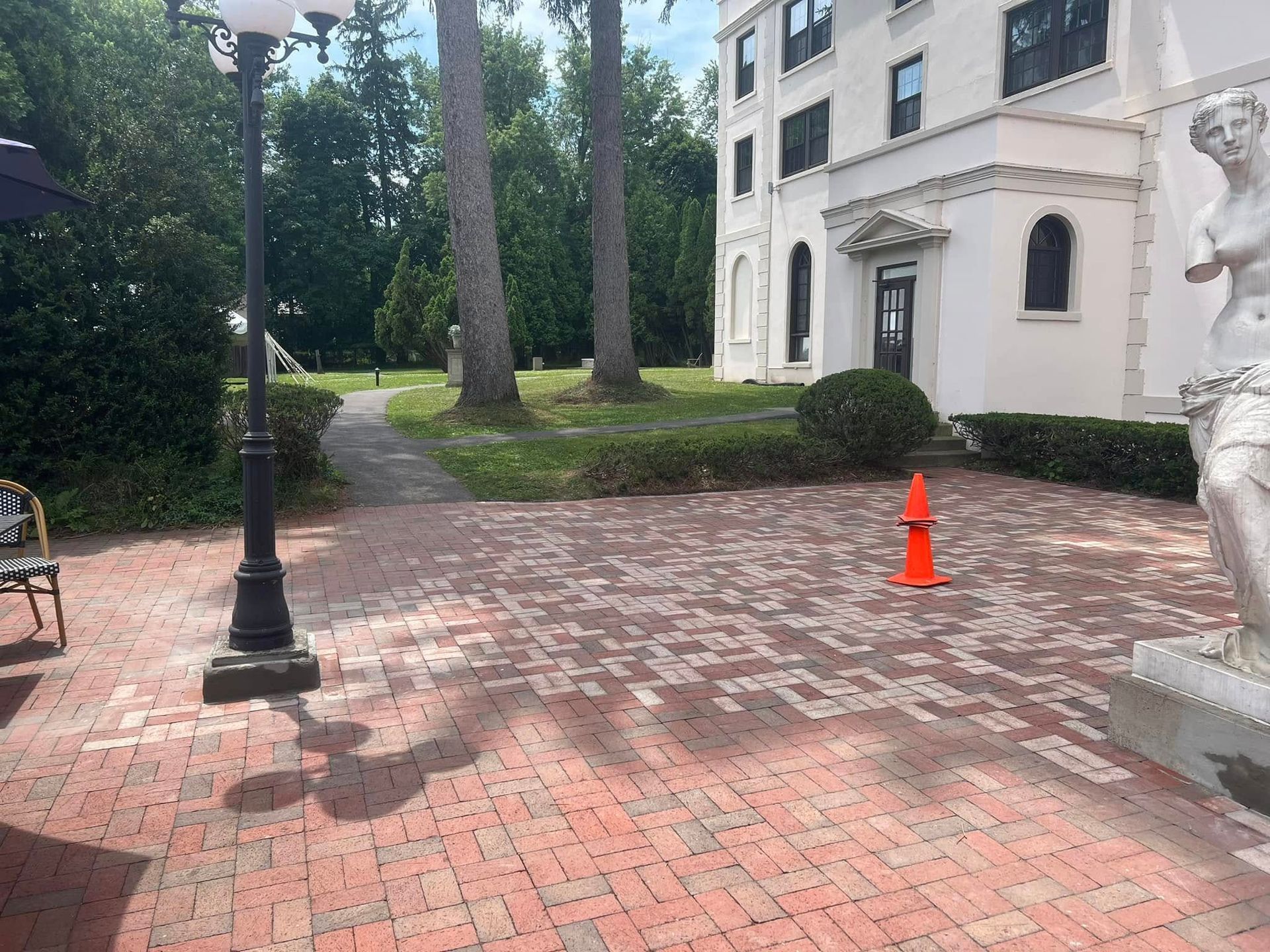 Brick patio with an orange traffic cone, statue, and ornate white building.