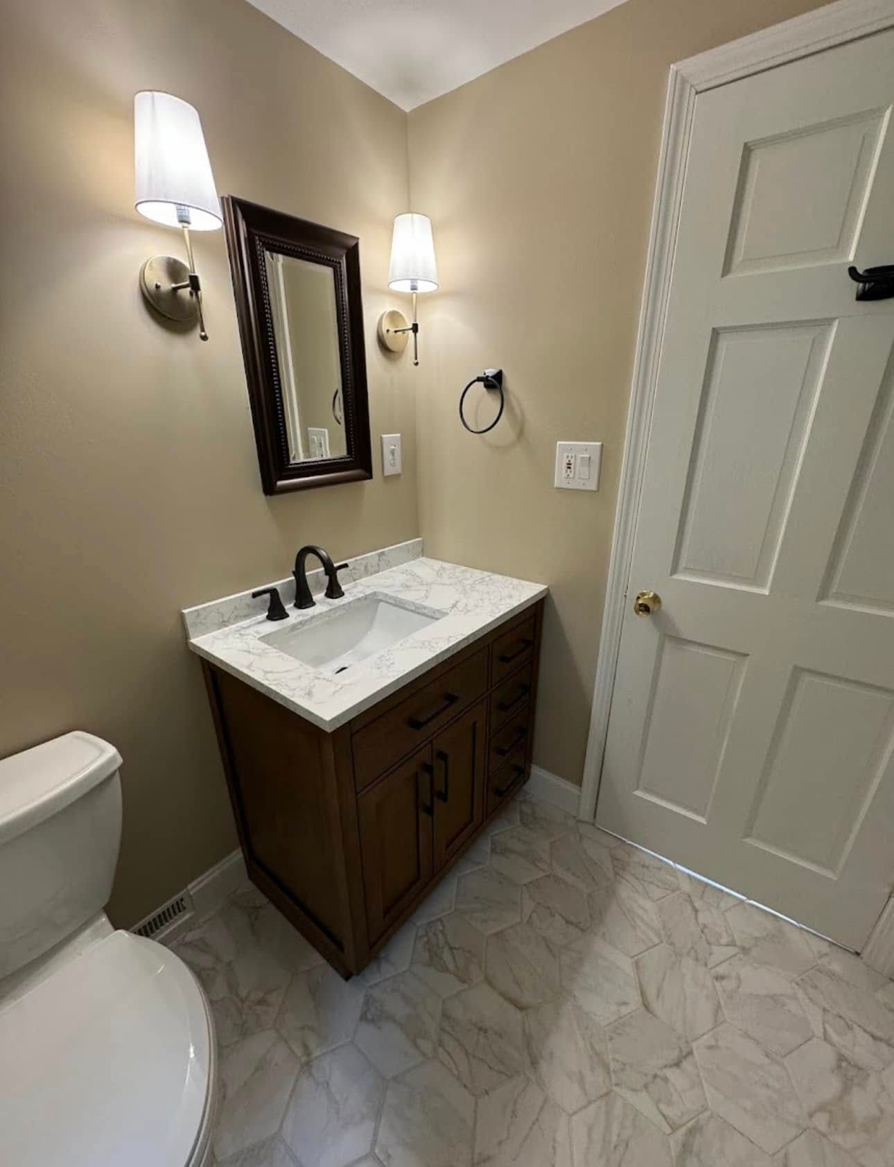 Small bathroom with a dark vanity, marble floors, and off-white walls.