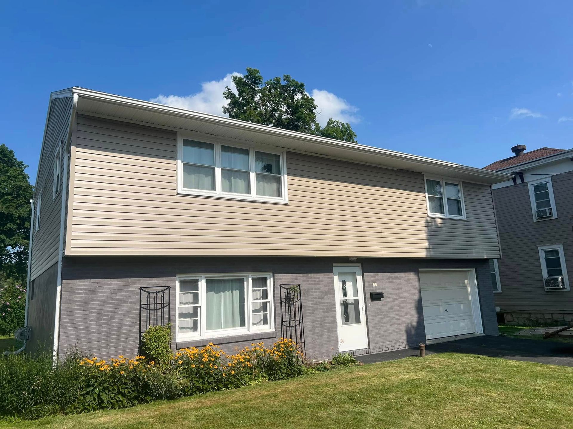 Two-story house with light-colored siding and a brick lower level, on a sunny day.
