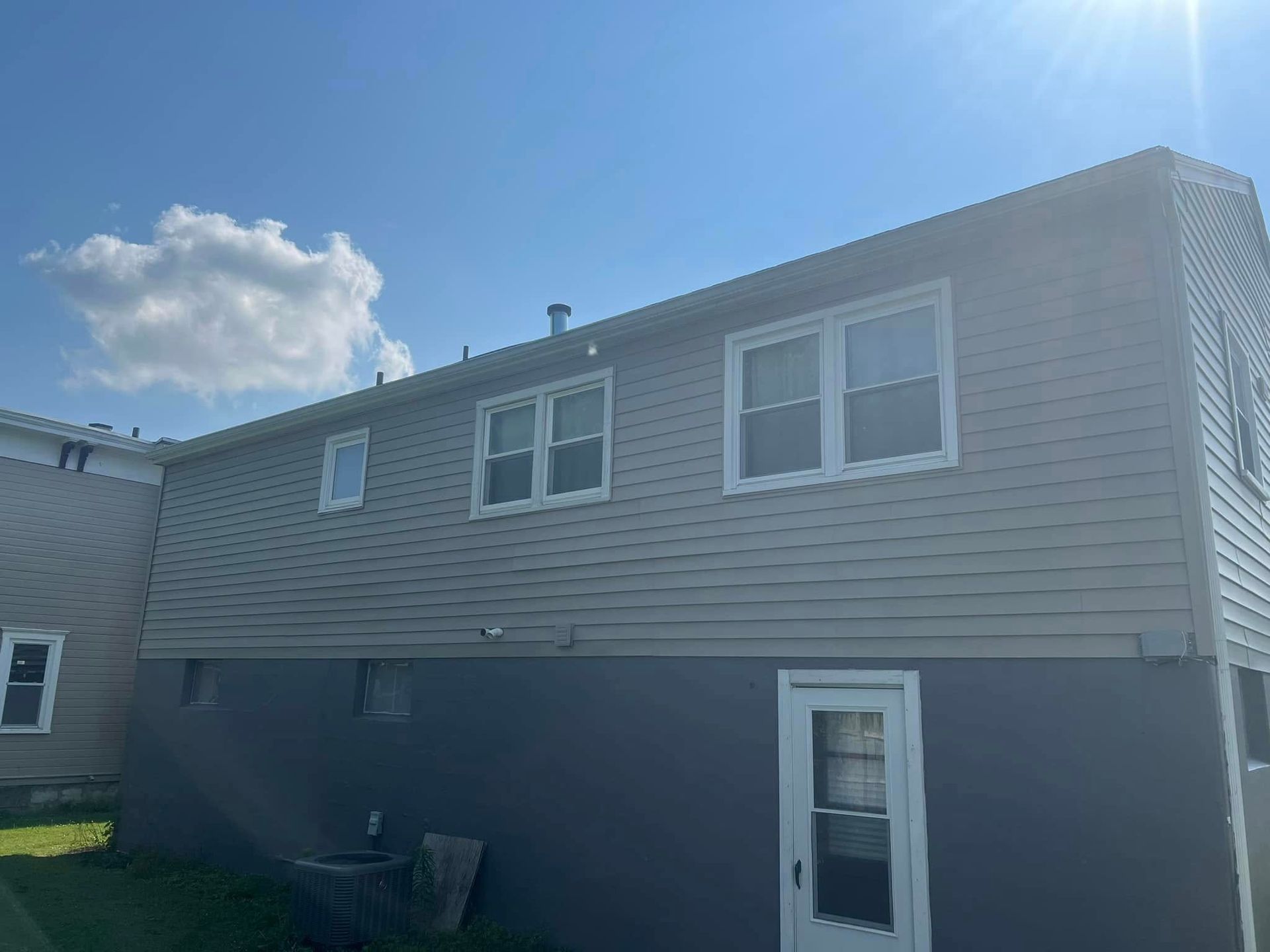 Side view of a two-story house with grey siding and dark blue foundation. A white door and windows are visible.