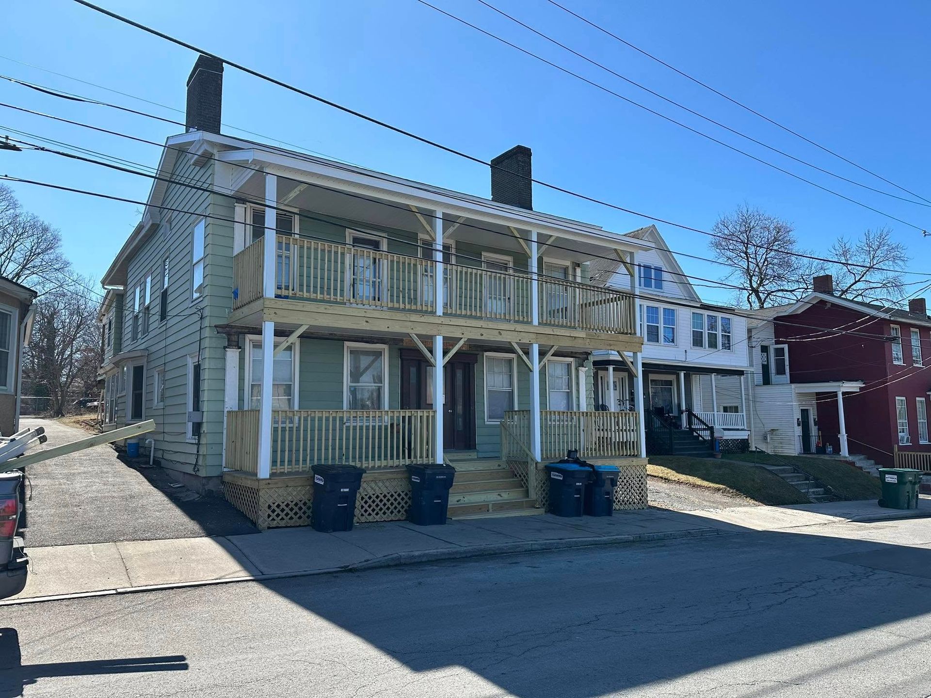 Two-story light green building with two porches; blue sky overhead; parked cars and street below.