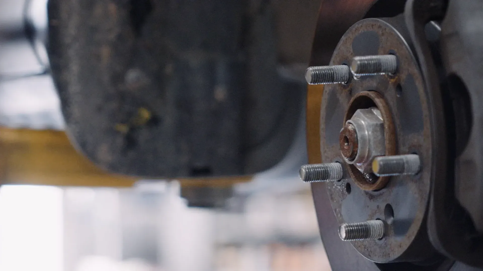Close-up of a car's rusty wheel hub with lug nuts, inside a repair bay.