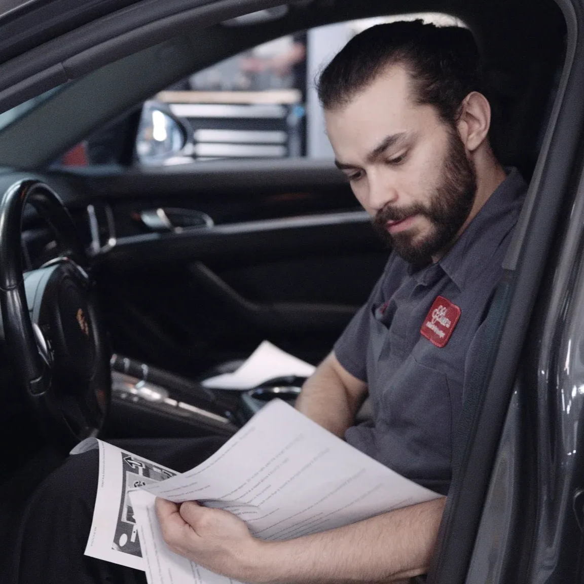 Mechanic in gray uniform, reviewing paperwork inside a car.