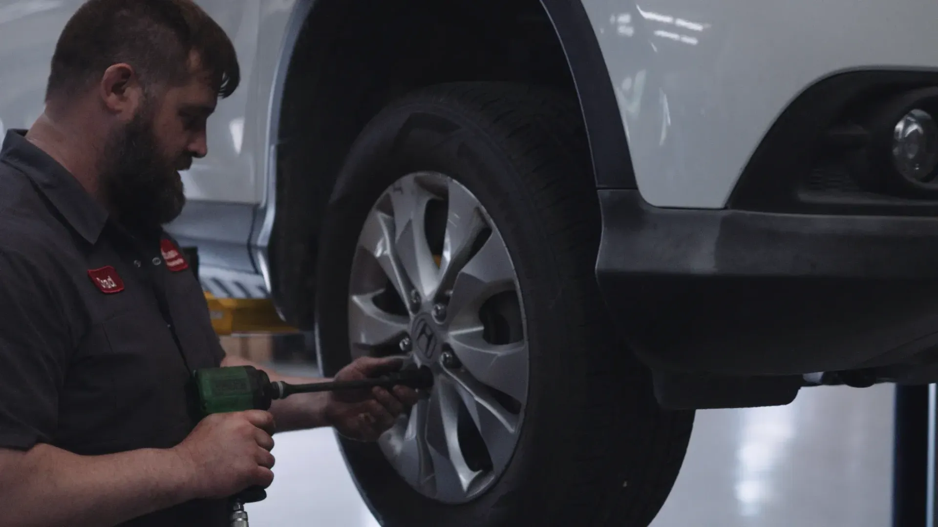 Mechanic using a power tool to remove a car's wheel in a service bay.