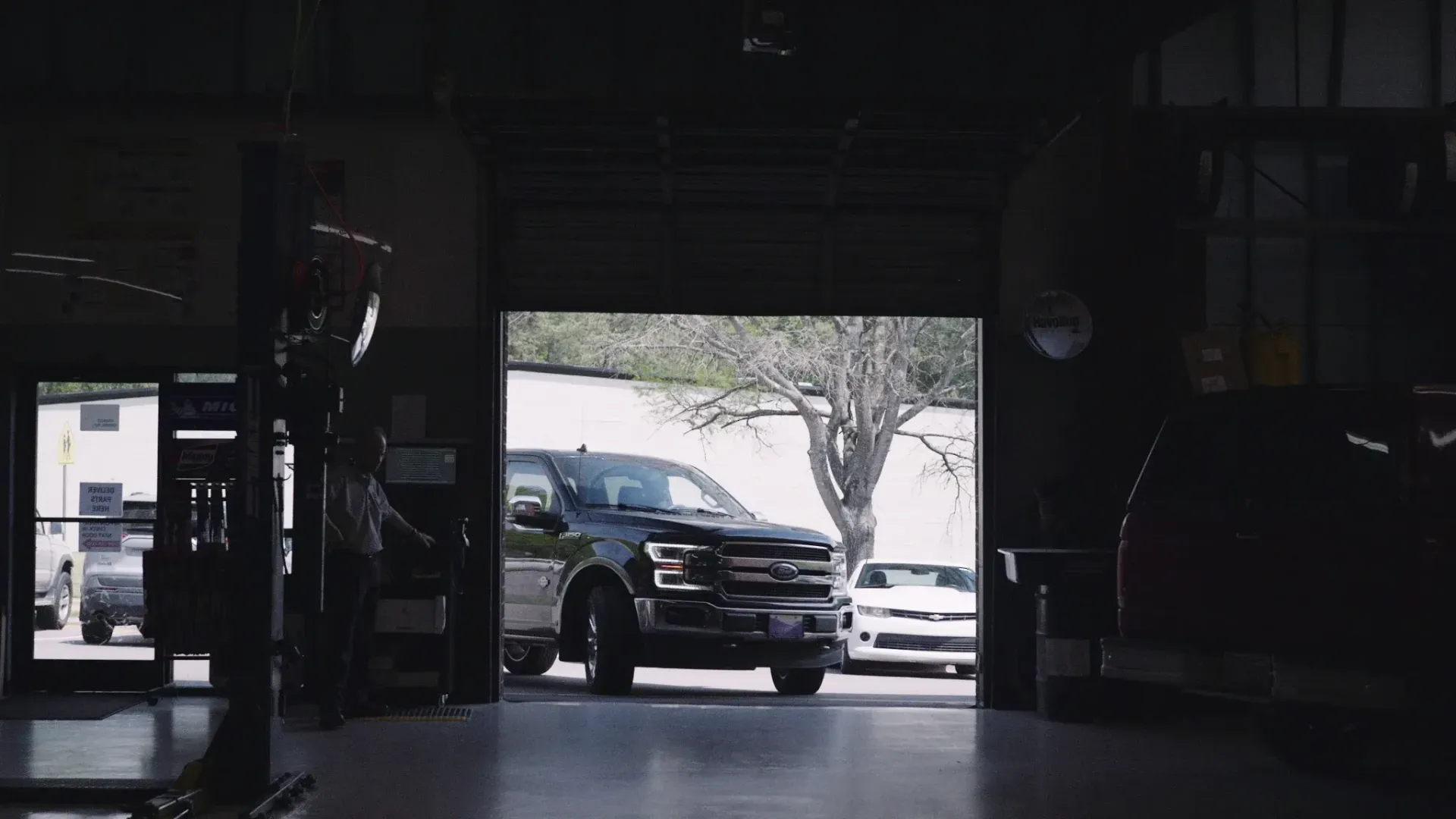Dark garage opening to reveal a black pickup truck and a white sports car.