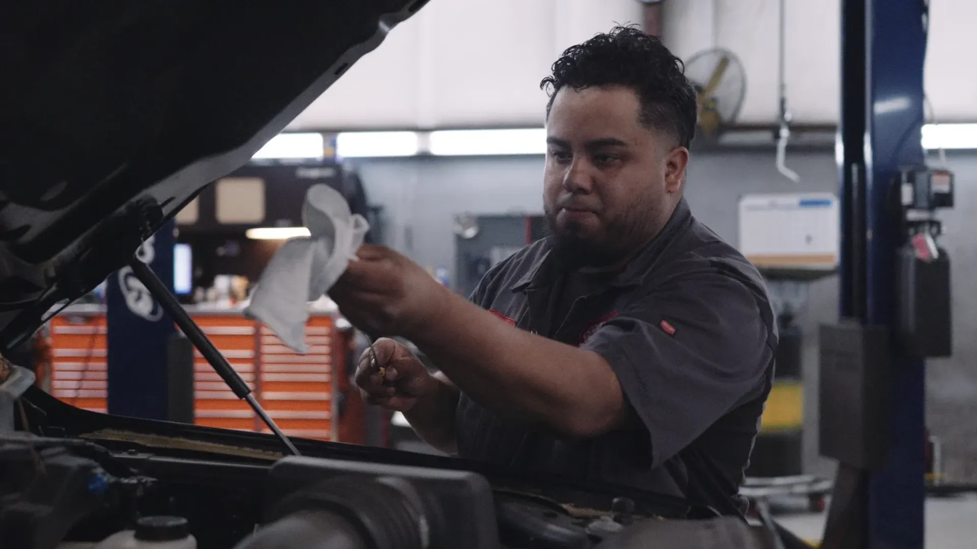 Mechanic checking engine oil with a rag in an auto shop.