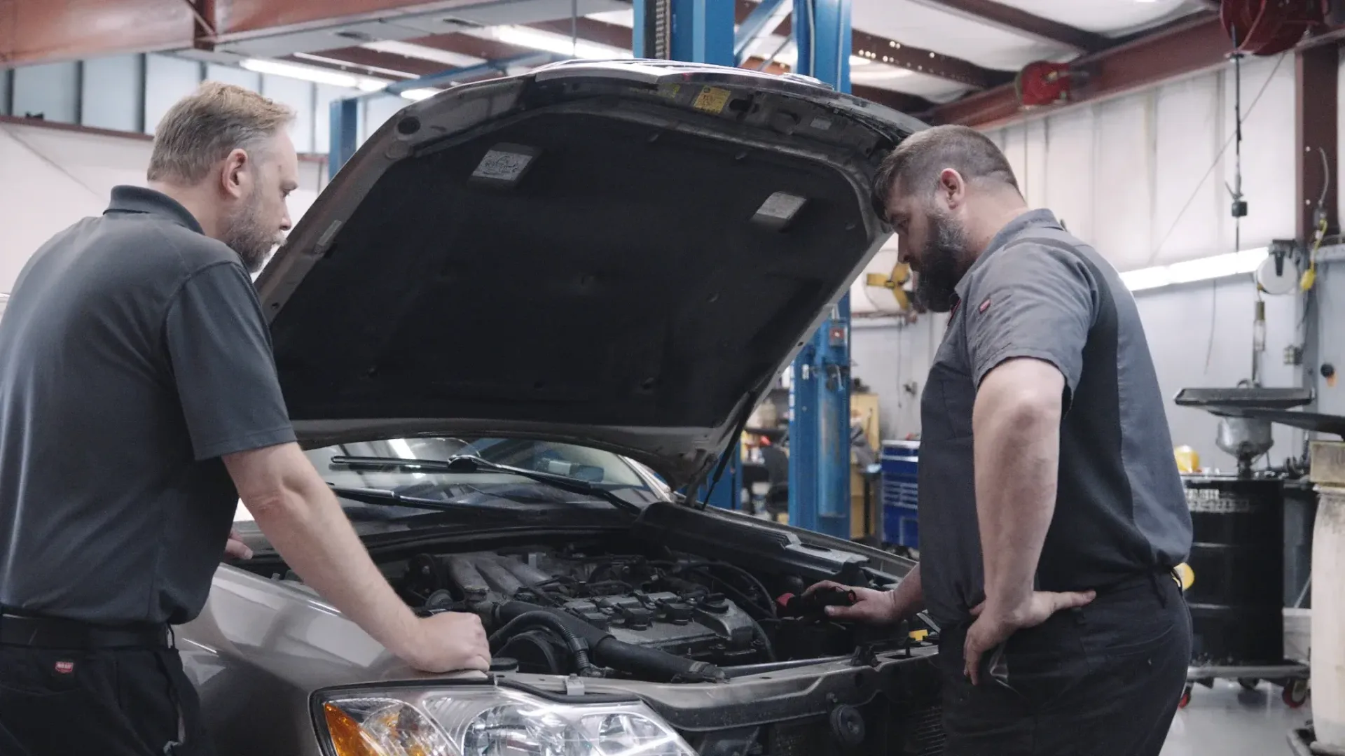 Two mechanics examining a car engine in an auto repair shop.