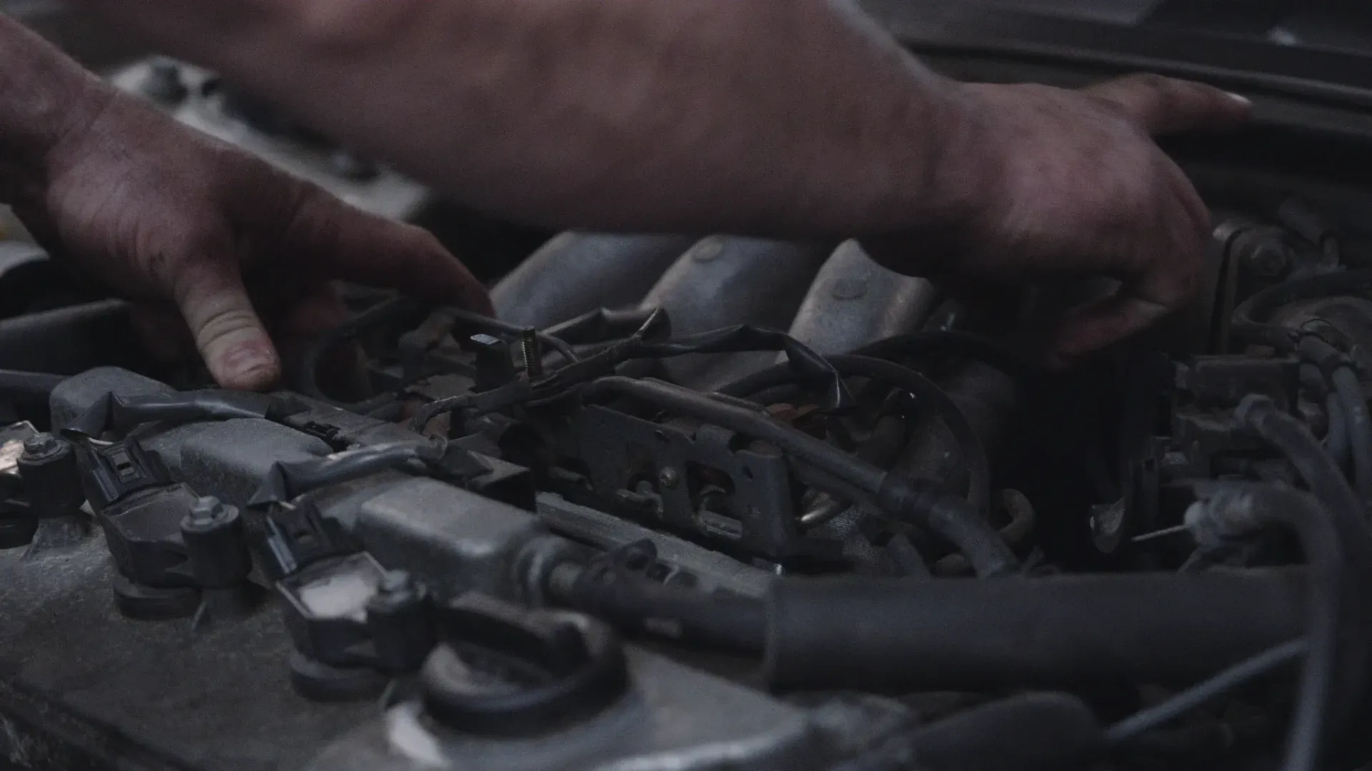 Hands working on a car engine, possibly repairing or inspecting components.