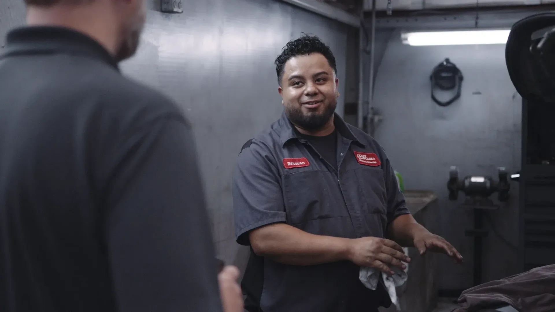 Man in mechanic uniform talking to another person in a shop.