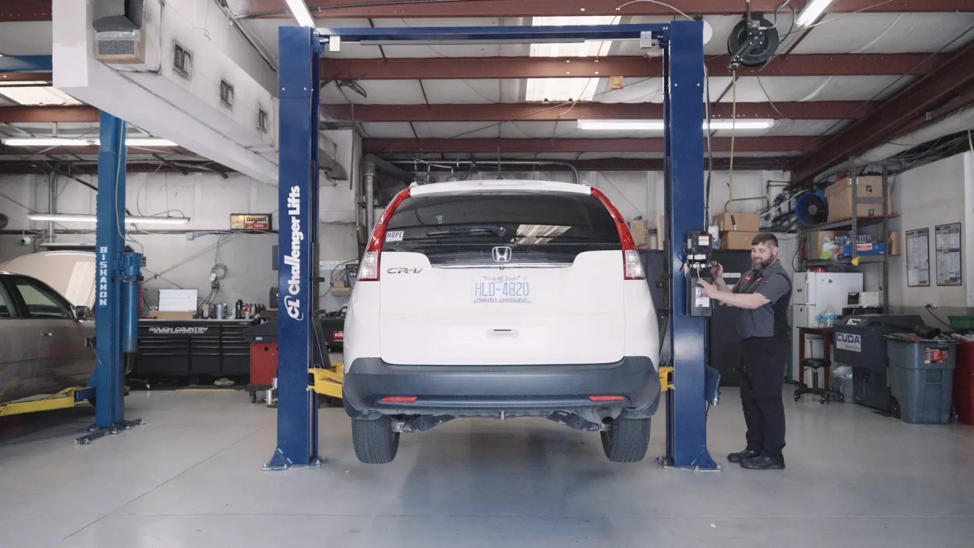 Mechanic raises white SUV on a lift in a garage.