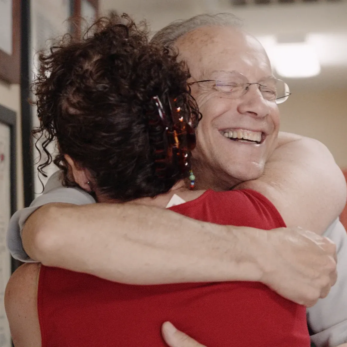 Man and woman embracing indoors; smiling, joyful expressions.