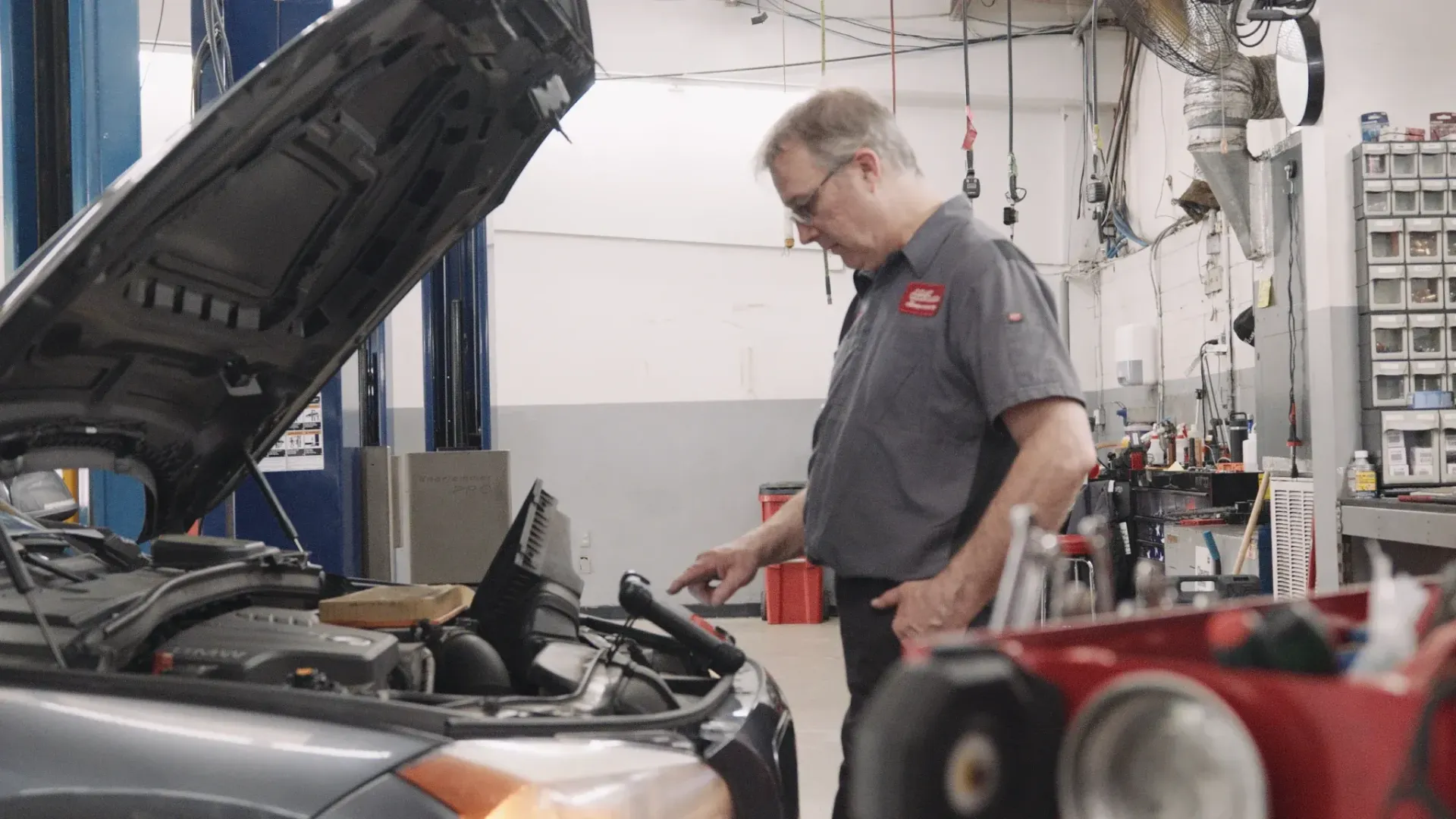 Mechanic working on car with hood open in auto shop.